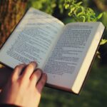 someone holding and reading a book outside near a tree